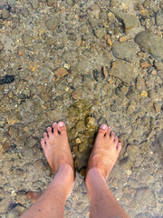 Relaxing barefoot in shallow water with smooth pebbles and sand underfoot for summer