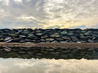 Stunning rock barrier reflects cloudy sky in calm water, peaceful landscape scene