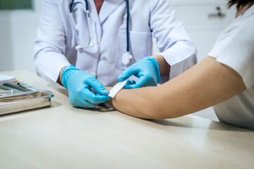 A male doctor wearing a white coat and blue medical gloves carefully bandages a patient’s arm, showing professionalism, hygiene, and compassion during wound treatment in a modern healthcare clinic