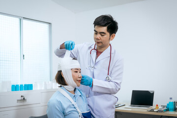 A male Asian doctor carefully adjusts the bandage on a female patient’s head, who also wears an arm sling, indicating multiple injuries requiring attentive care  comprehensive medical rehabilitation