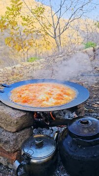 Traditional outdoor cooking with omelet (egg and tomato dish, Iranian food) in a large metal pan over open fire, kettle and teapot preparing fire tea in rural nature.
📍Hawraman Takht, Kurdistan 