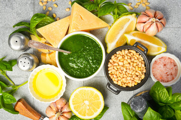 Ingredients for making Pesto sauce: basil, parmesan, nuts, lemon and spices. On a gray stone background.