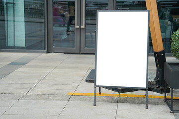 Blank white outdoor advertising stand sandwich board mock up template. Clear street signage board placed by an outdoor dinning area of a restaurant.