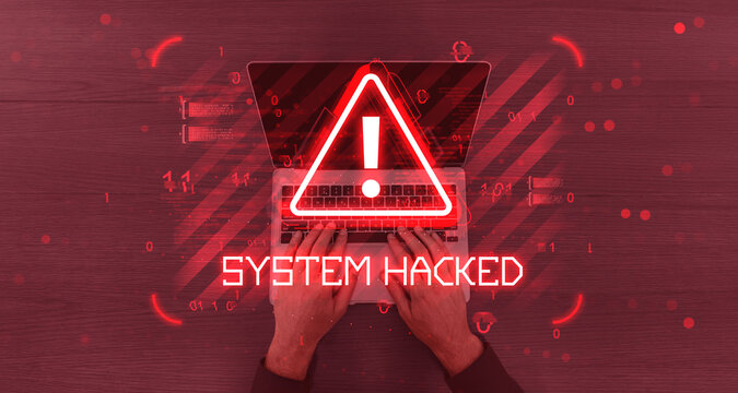 Cybersecurity alert with red warning sign and text "System Hacked" over hands typing on laptop with digital glitch effect on wood background.