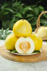 Fresh Sweet Yellow Melons on Wooden Board with Natural Kitchen Setting and Green Plant Background