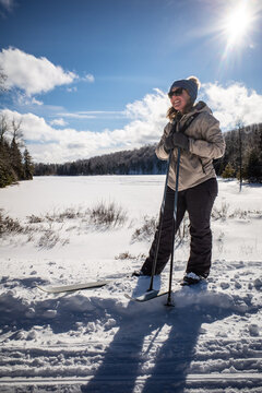 Female cross country skier pauses in front of a snow covered lake
