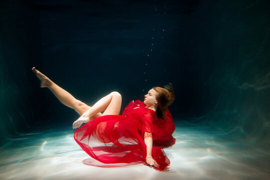 Woman in red dress swims gracefully underwater in clear pool