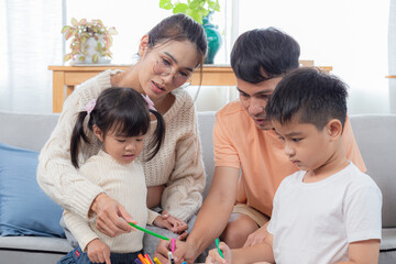 Obraz premium Young Asian parents help their children with homework. mom and dad teach daughter and son to draw and paint. Happy family spending free time together on holidays, activity at home.