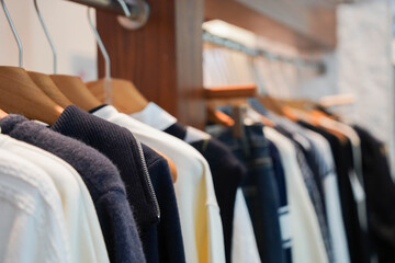 Multi-colored warm knitted sweaters hang on wooden hangers in clothing store.