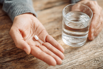 Senior person taking medicine with glass of water on wooden table for health care and treatment concept