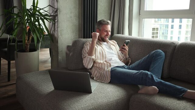 Casual man using phone in modern bright living room.