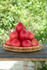 Fresh Red New Zealand Pears in Wicker Basket on Rustic Wooden Table with Green Natural Background