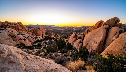 Rugged Desert Landscape at Dusk Featuring Large Rock Formations and Distant Town Lights Under a Warm Hued Sky