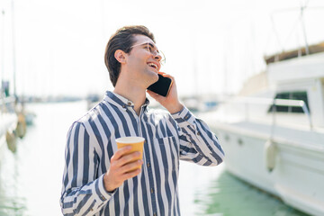 Young handsome man using mobile phone and holding a coffee with happy expression