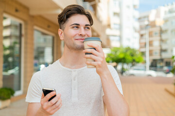 Young handsome man using mobile phone and holding a coffee