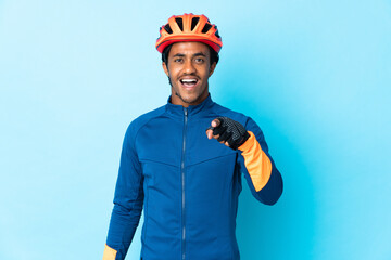 Young cyclist man with braids over isolated background surprised and pointing front