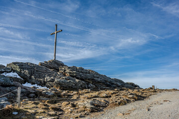 Holzkreuz auf einem felsigen Gipfel unter blauem Himmel am Nachmittag