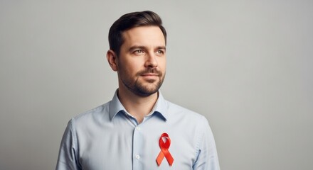 A hopeful-looking man with a beard, wearing a red awareness ribbon on his shirt for HIV/AIDS support.
