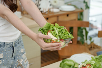 Closeup of multiracial teenage girl's hands presenting fresh salad bowl in kitchen focusing on natural healthy food and lifestyle for beauty skincare through vegetable rich nutrition and clean eating