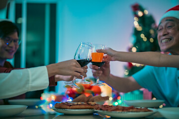 Close-up wine glass clinking with orange juice. Family enjoying holiday dinner, clinking wine glasses in celebration, creating a warm and joyful Christmas moment together.