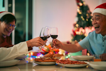 Close-up of hands holding wine glasses making a toast during a family Christmas celebration with food, laughter, and festive bokeh lights.