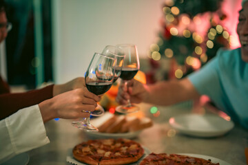 Close-up of Asian family toasting red wine together during Christmas celebration at home, surrounded by warm lights, pizza, and festive holiday decorations.