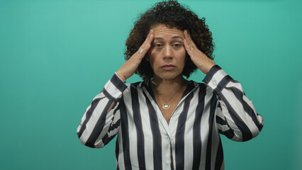 Woman middle aged in striped shirt pressing temples with both hands and closed eyes in studio; stress.
