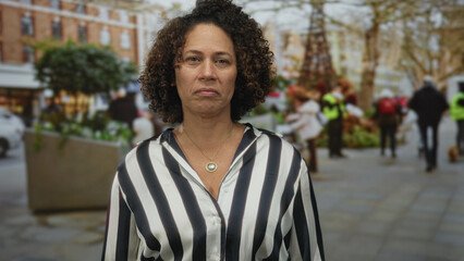 Woman looking at camera with visible necklace on a busy street plaza near planter box and blurred...