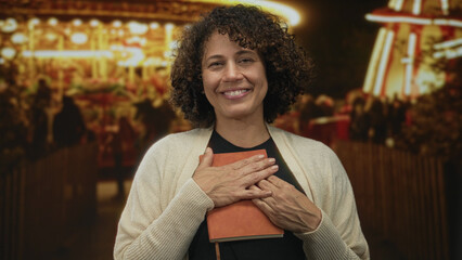 Woman holding leather journal close to chest at night street fair under glowing lights; serenity...