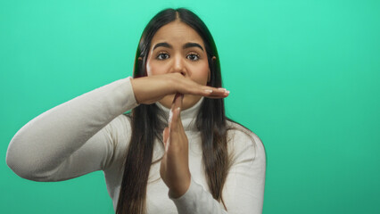 Young woman signaling timeout over isolated green background suggesting pause or break in communication or activity in a casual setting.