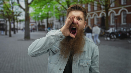 Bearded man cups hand to mouth shouting on a cobblestone city street with blurred pedestrians and parked motorcycles; anger protest call defiance.