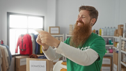 Young bearded man wearing green shirt claps hands beside donation box in donation building; generosity.