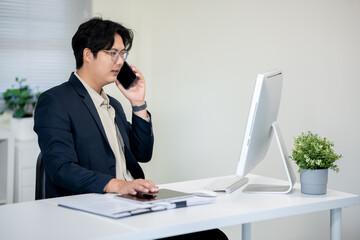 Male office worker talking on the phone with a customer at a computer desk in the office.