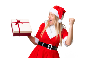 Young blonde woman with christmas hat and holding a gift over isolated chroma key background celebrating a victory