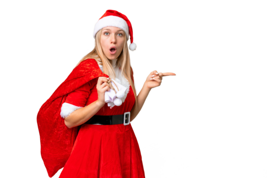 Young blonde woman with christmas hat over isolated chroma key background surprised and pointing side