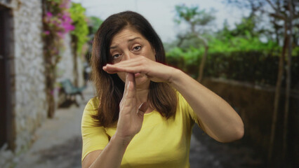 Woman makes time out gesture with hands on urban street lined with bougainvillea and stone wall in daylight; pause contemplation.
