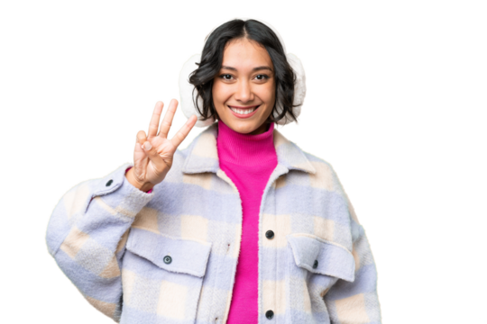 Young Argentinian woman wearing winter muffs over isolated background happy and counting three with fingers