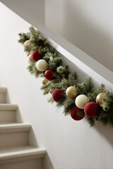 beautifully arranged christmas garland adorned with colorful ornaments rests against pristine white wall