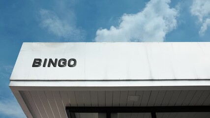 Bingo word sign brightly displayed on the exterior of an entertainment or community hall building beneath a clear blue sky, signifying a venue for games, socializing, and charitable fundraising