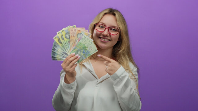 Young woman holding romanian banknotes over a vibrant purple background, smiling confidently to convey wealth and financial success.