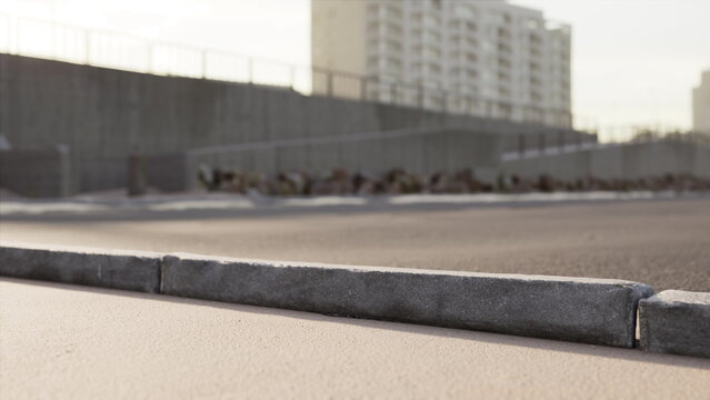 Newly constructed pavement is visible in a busy area, with tall buildings lining the background. The sun shines, casting a warm glow over the smooth surface, indicating recent work.
