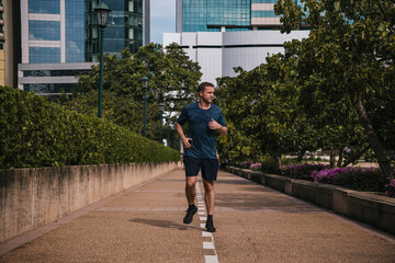 Man jogging along an urban park path, showcasing fitness, determination and healthy active lifestyle amid trees and city backdrop