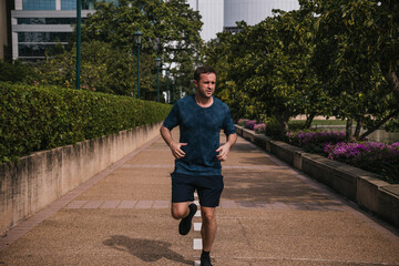 Fototapeta premium Man running on a path in a green city park, actively pursuing fitness and a healthy, energetic lifestyle outdoors