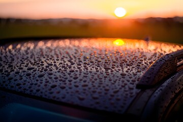Fototapeta premium Water droplets on car roof with sunset reflecting creating a beautiful background scene