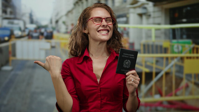 Fototapeta Woman with italian passport at a construction site, excitedly pointing to the side with a bright smile outdoors in an urban city environment.