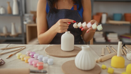 Woman with red nails points finger to paint pots over a ceramic vase in studio; creativity serenity.