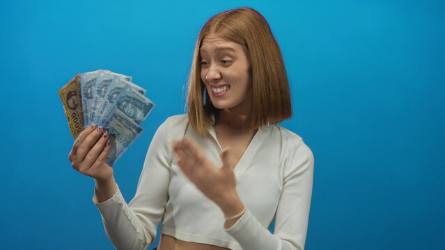 Young woman with blonde hair excitedly holding hungarian forint banknotes against a blue background, expressing surprise and delight with wide eyes and open mouth.
