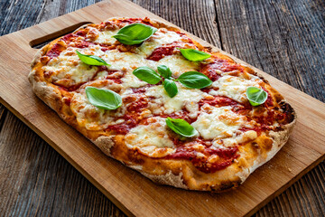 Pinsa Margherita with tomato sauce, basil leaves and mozzarella cheese on wooden background