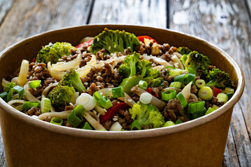 Lunch in disposable box. Takeaway Chow Mein noodles with ground beef, broccoli and red bell pepper on wooden table	
