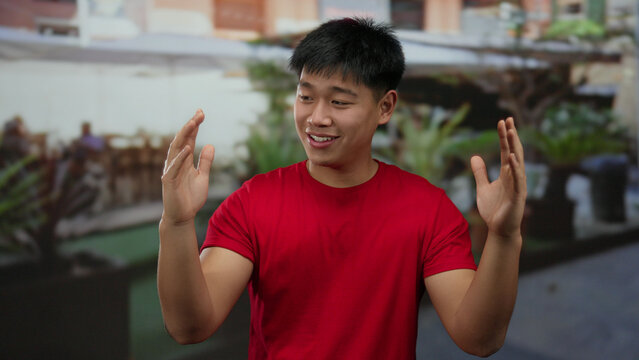 Young man in a red shirt gesturing on an outdoor terrace at a restaurant, illustrating a lively conversation in a vibrant coffee shop environment. - Powered by Adobe